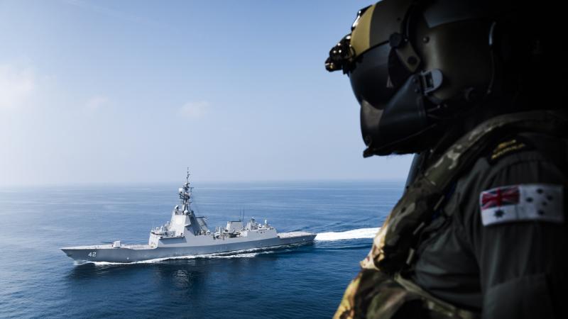 An ADF member in uniform looks out to the water where there is a large boat.