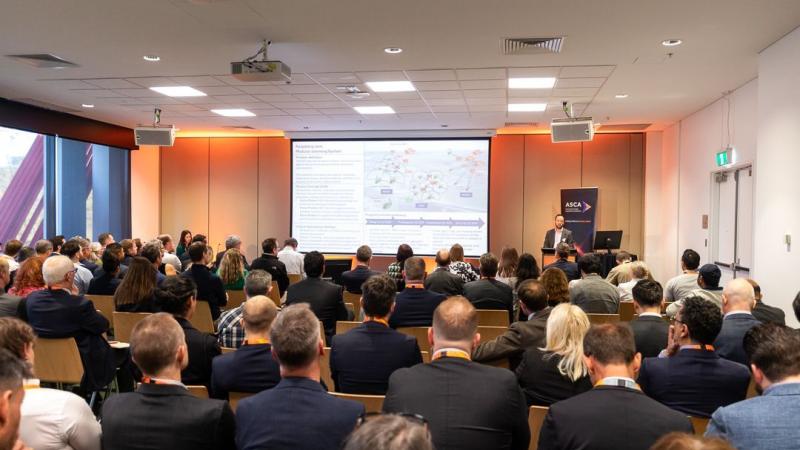 Room shot of the ASCA Pitch Day 2024, including a presenter, their slides and the audience. 